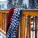 Two buffalo check robes, draped over a wooden railing with a snowy landscape and trees in the background in Banff, Canada