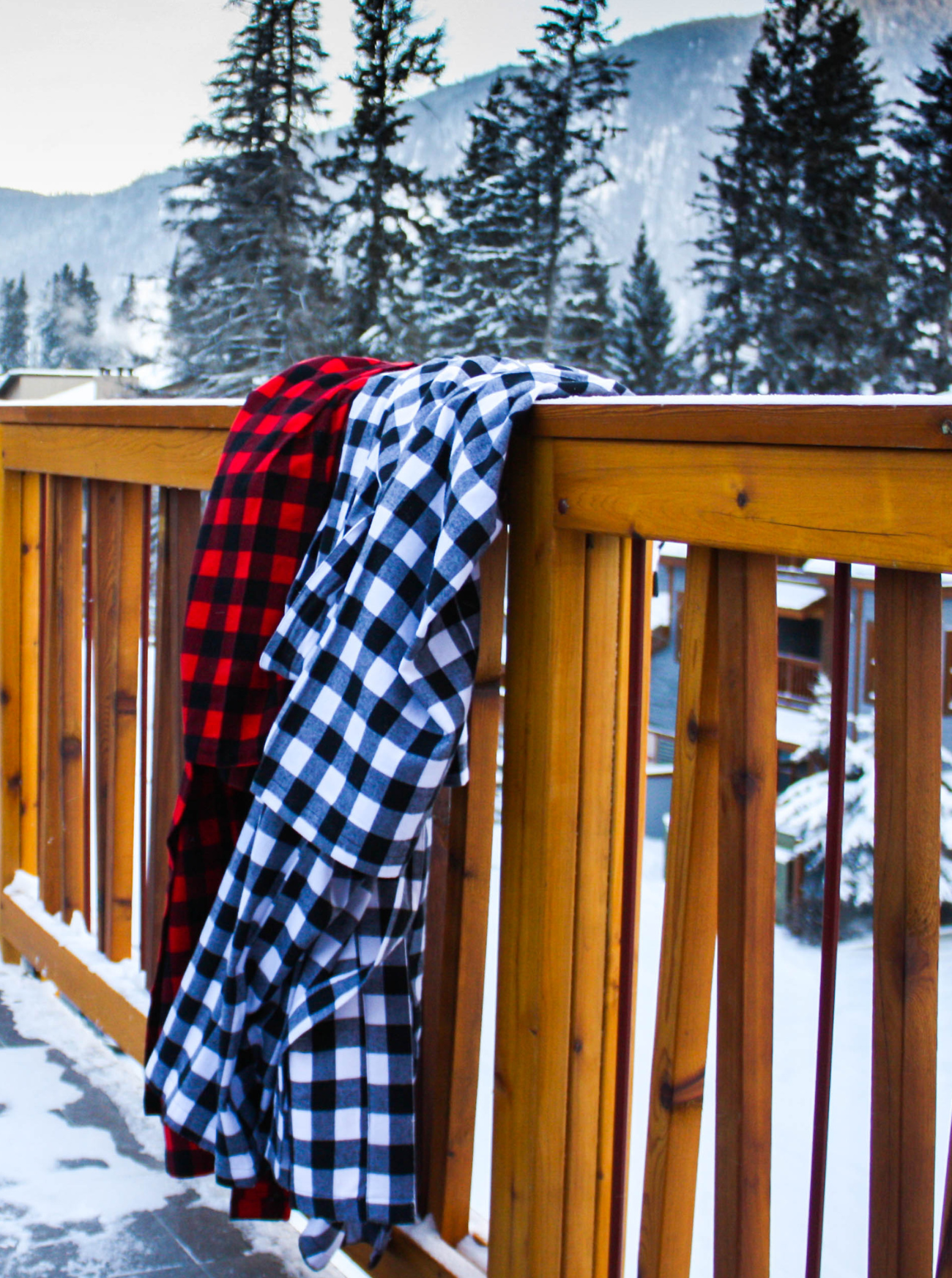 Two buffalo check robes, draped over a wooden railing with a snowy landscape and trees in the background in Banff, Canada