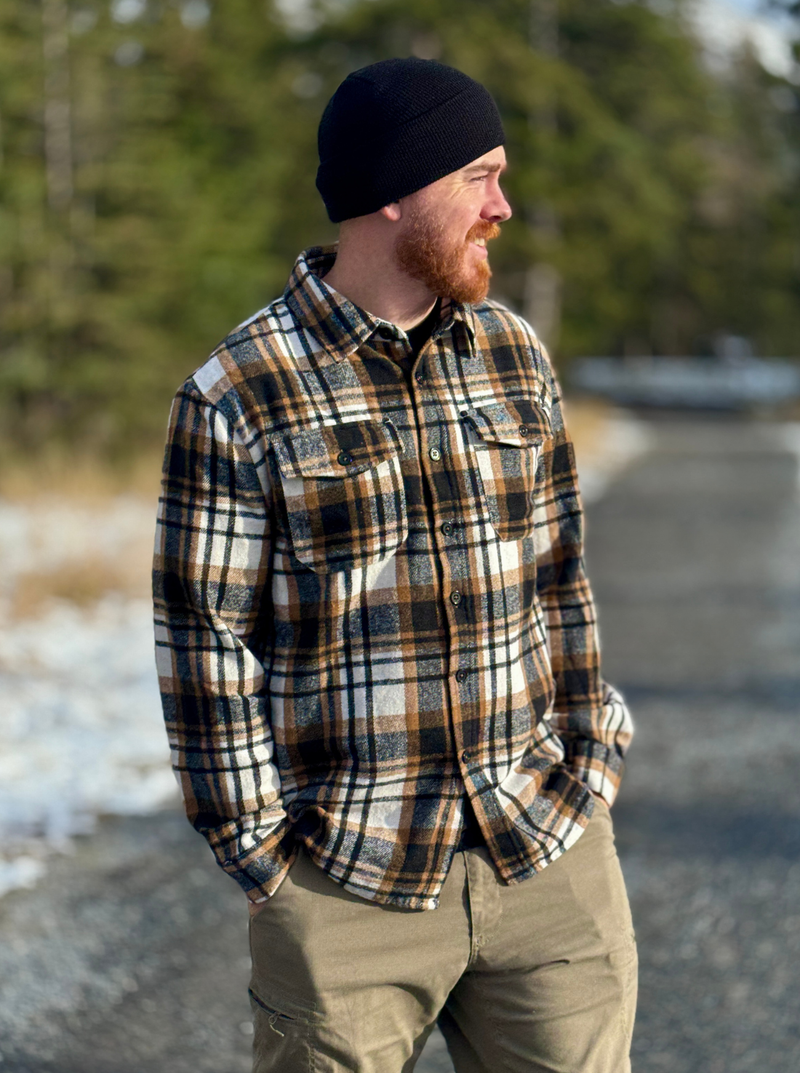 Man wearing a plaid jacketand black beanie standing outdoors with trees in the background