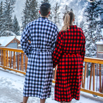 Two people wearing buffalo check robes standing on a snowy deck with mountains in the background in Banff, Canada