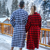 Two people wearing buffalo check robes standing on a snowy deck with mountains in the background in Banff, Canada