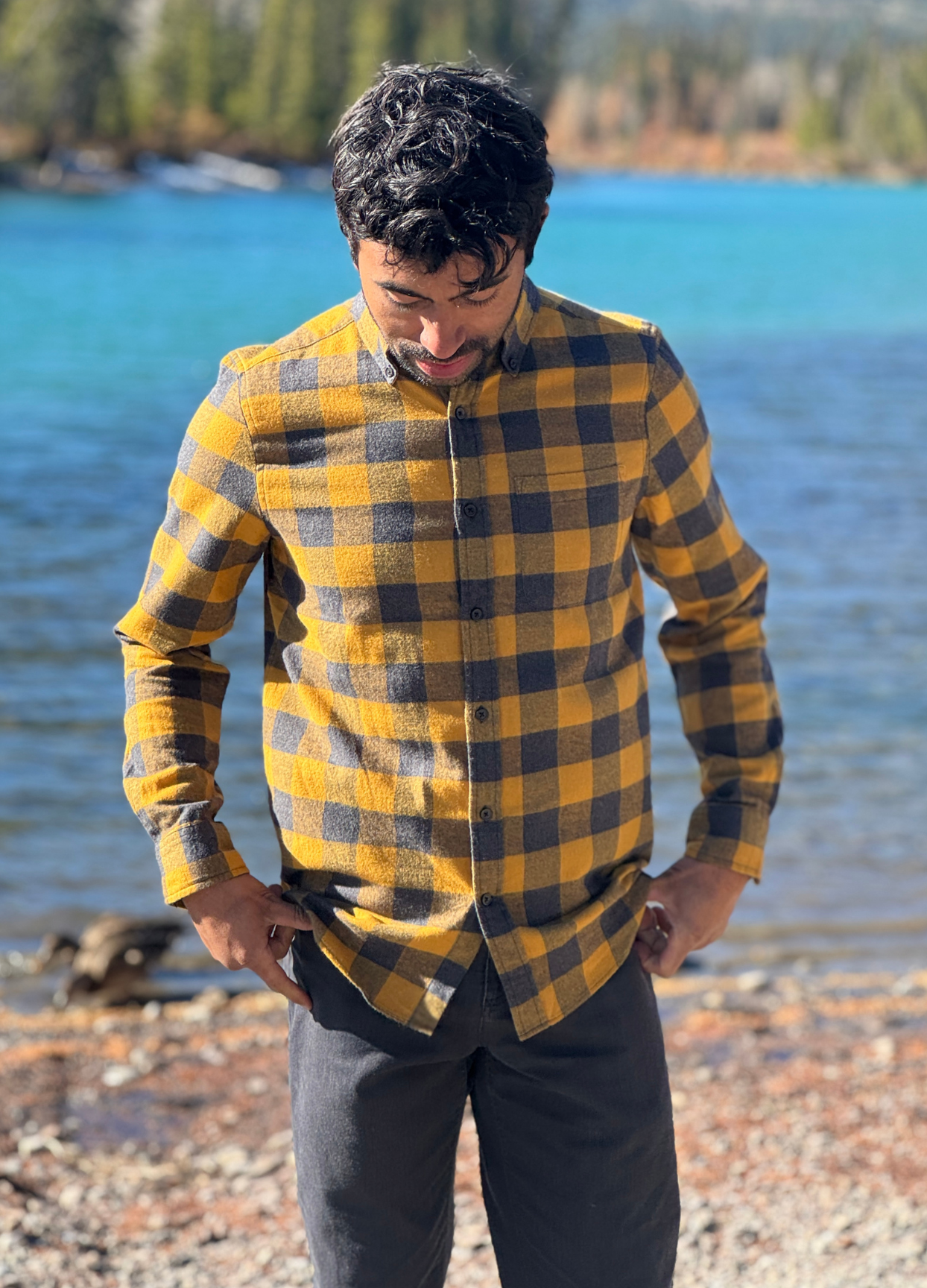 Man wearing a gold and grey buffalo check shirt by a river in Banff National Park