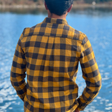 Person wearing a gold and grey checkered shirt standing by a river with mountains in the background in Banff National Park