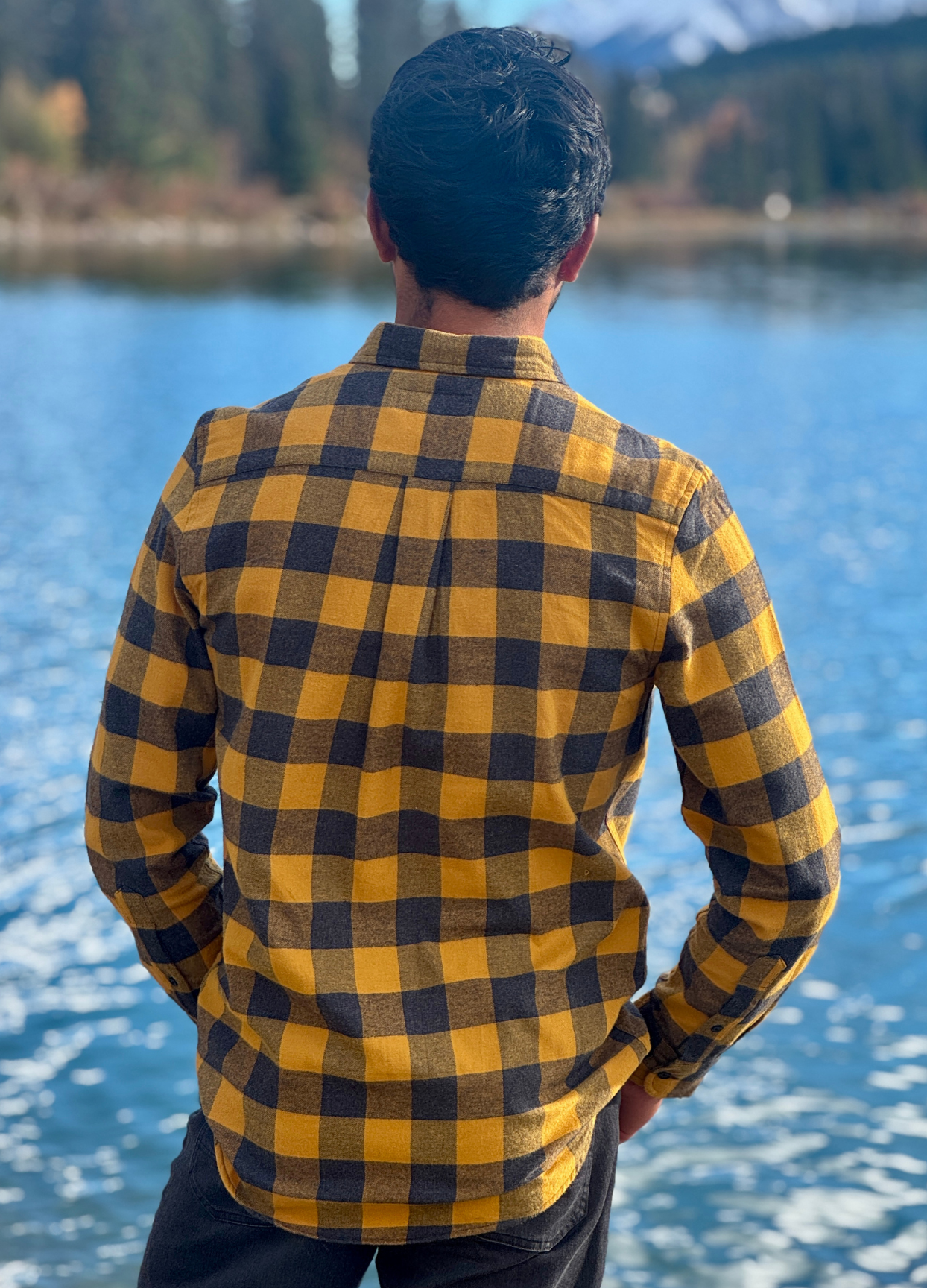 Person wearing a gold and grey checkered shirt standing by a river with mountains in the background in Banff National Park