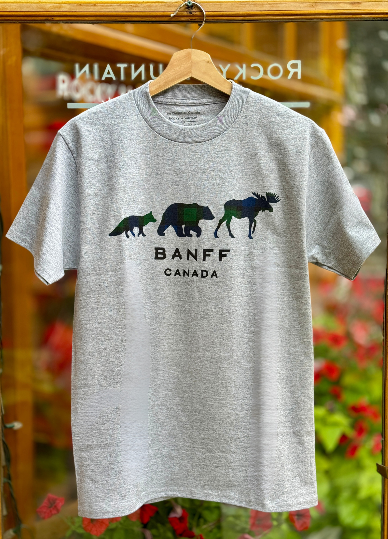 Grey t-shirt with bear and moose design and 'Banff Canada' text on a hanger.
