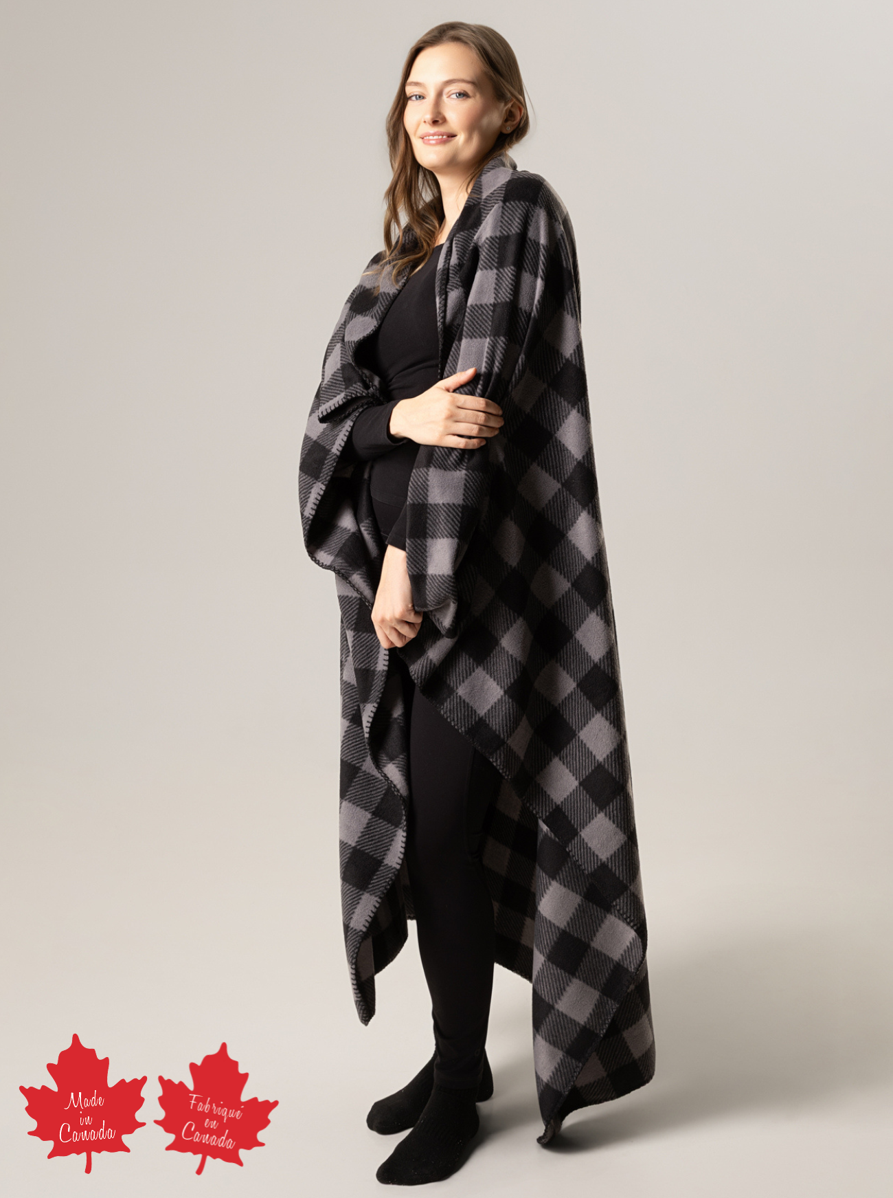 Woman wearing a black and grey checkered blanket with 'Made in Canada' label on a plain background