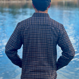 Person wearing a plaid shirt standing by a lake with mountains in the background