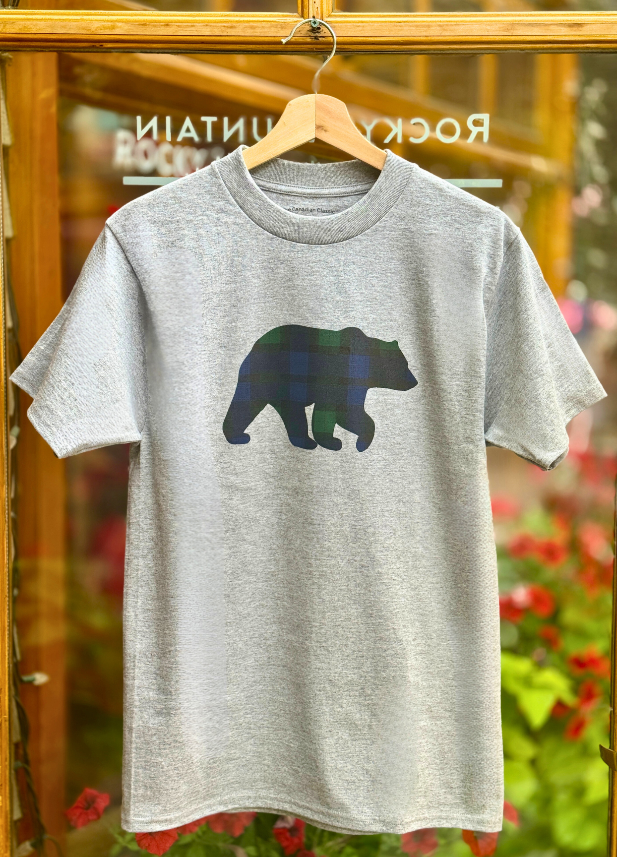 Grey t-shirt with a black watch bear graphic on a hanger against a blurred floral background