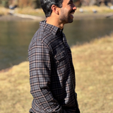 Man wearing a plaid flannel shirt standing by a river with trees in the background in Banff National Park