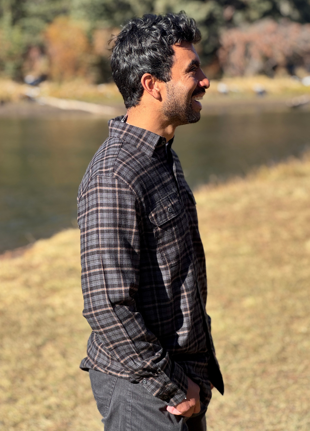 Man wearing a plaid flannel shirt standing by a river with trees in the background in Banff National Park