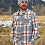 Man wearing a plaid shirt and beanie standing in a field with mountains in the background. Shot in Banff, Canada
