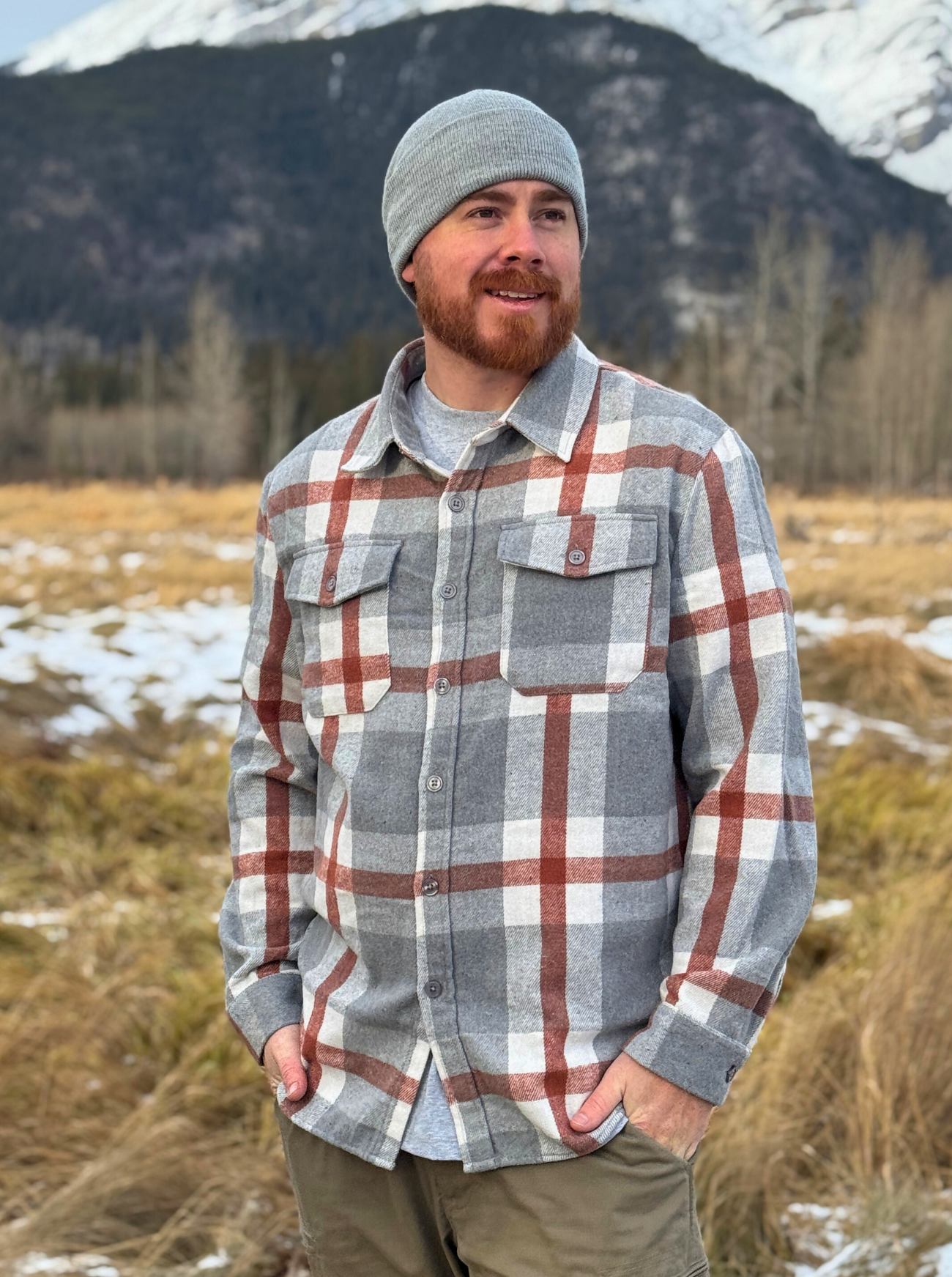 Man wearing a plaid shirt and beanie standing in a field with mountains in the background. Shot in Banff, Canada