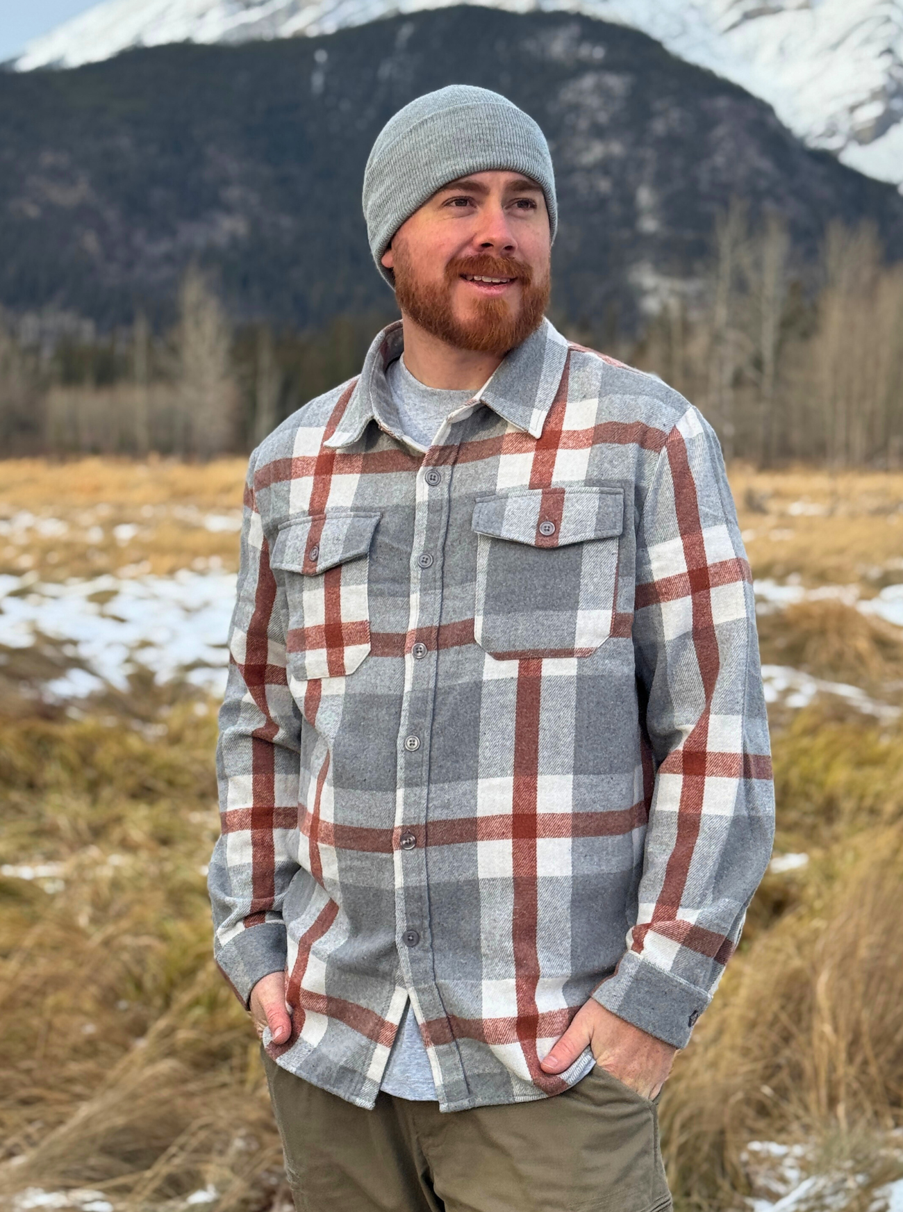Man wearing a plaid shirt and beanie standing in a field with mountains in the background. Shot in Banff, Canada