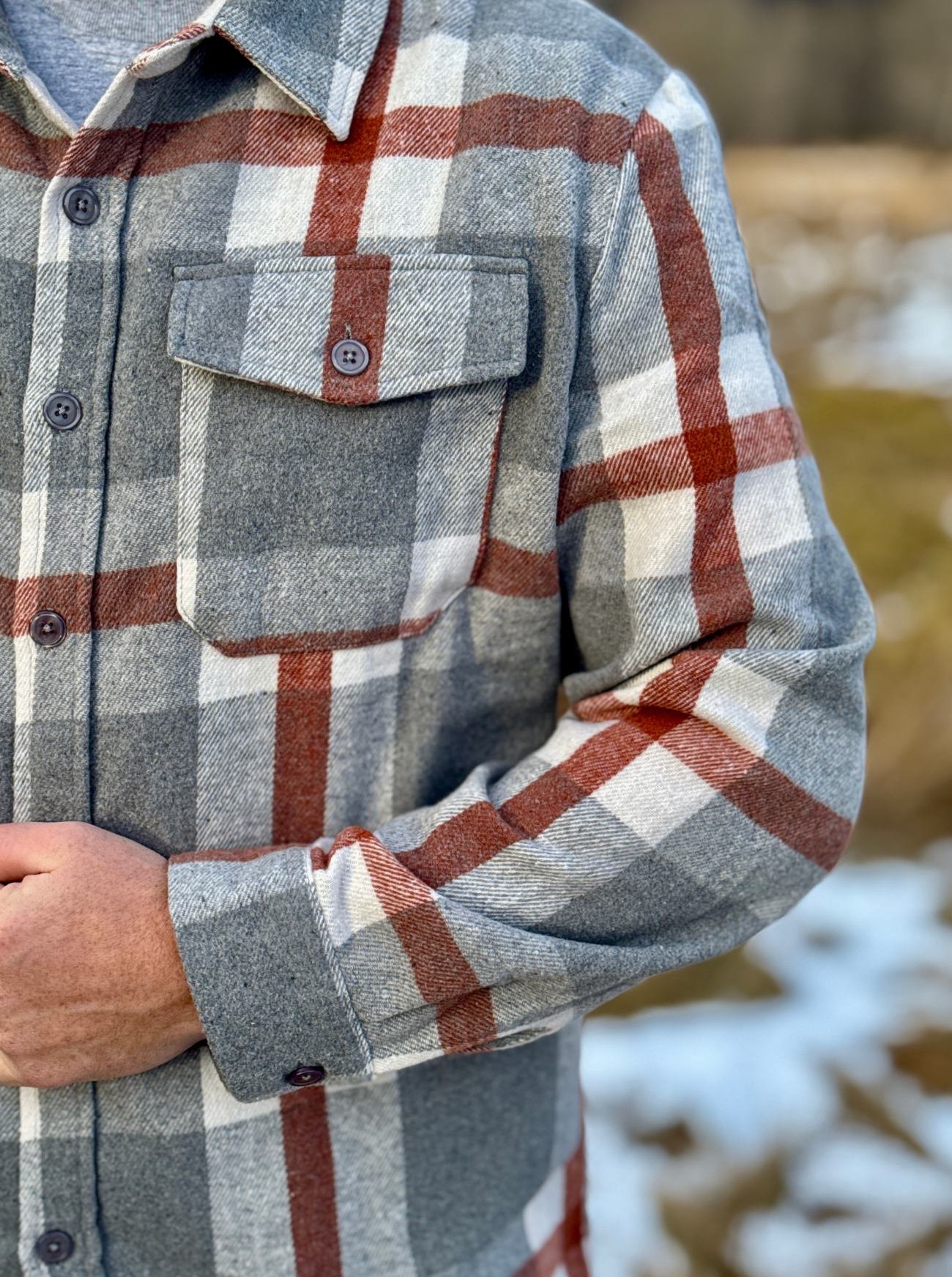 Plaid shirt with a focus on the chest pocket and sleeve, blurred natural background