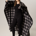 Woman holding a black and grey buffalo check blanket against a plain background