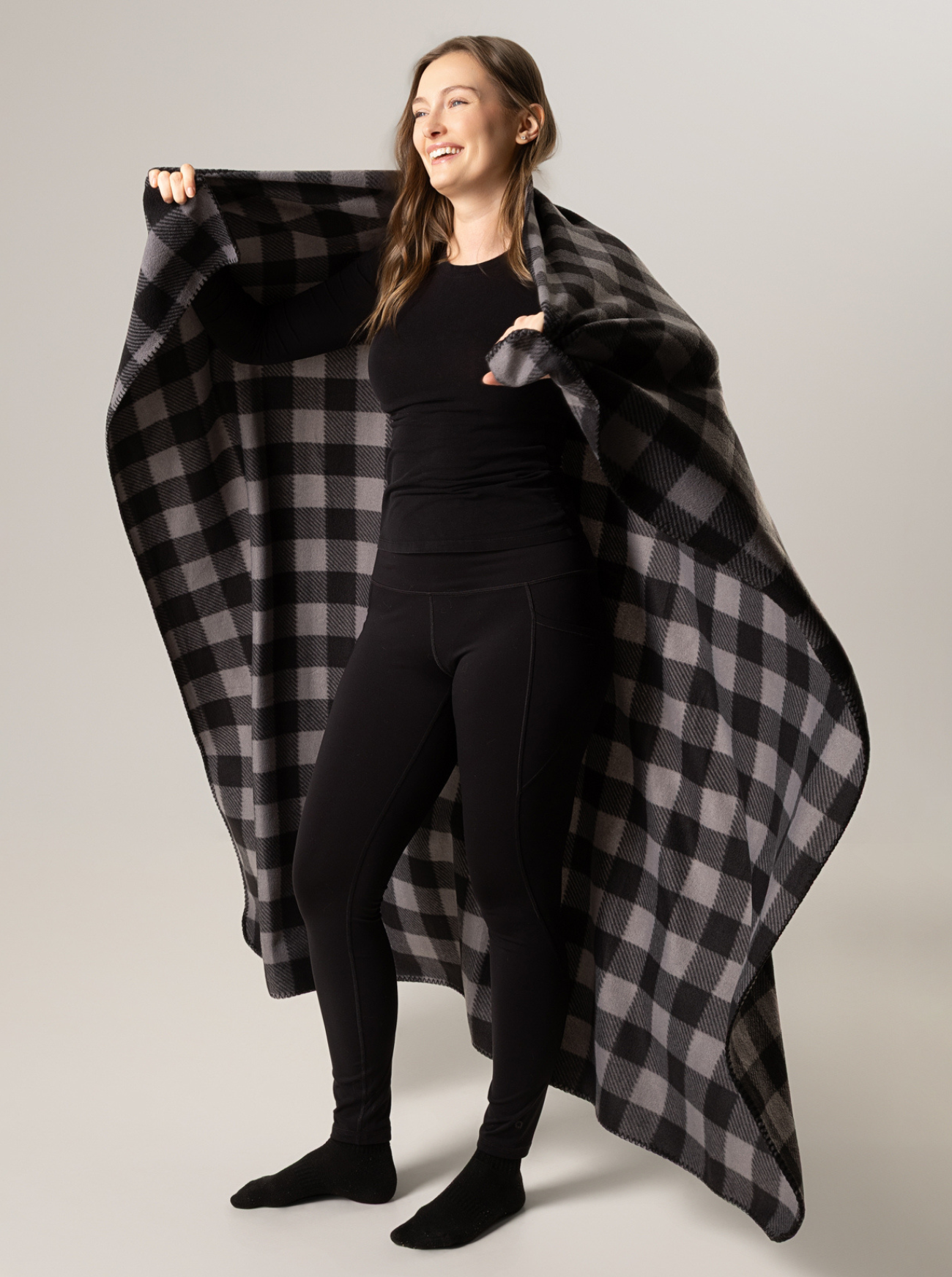 Woman holding a black and grey buffalo check blanket against a plain background