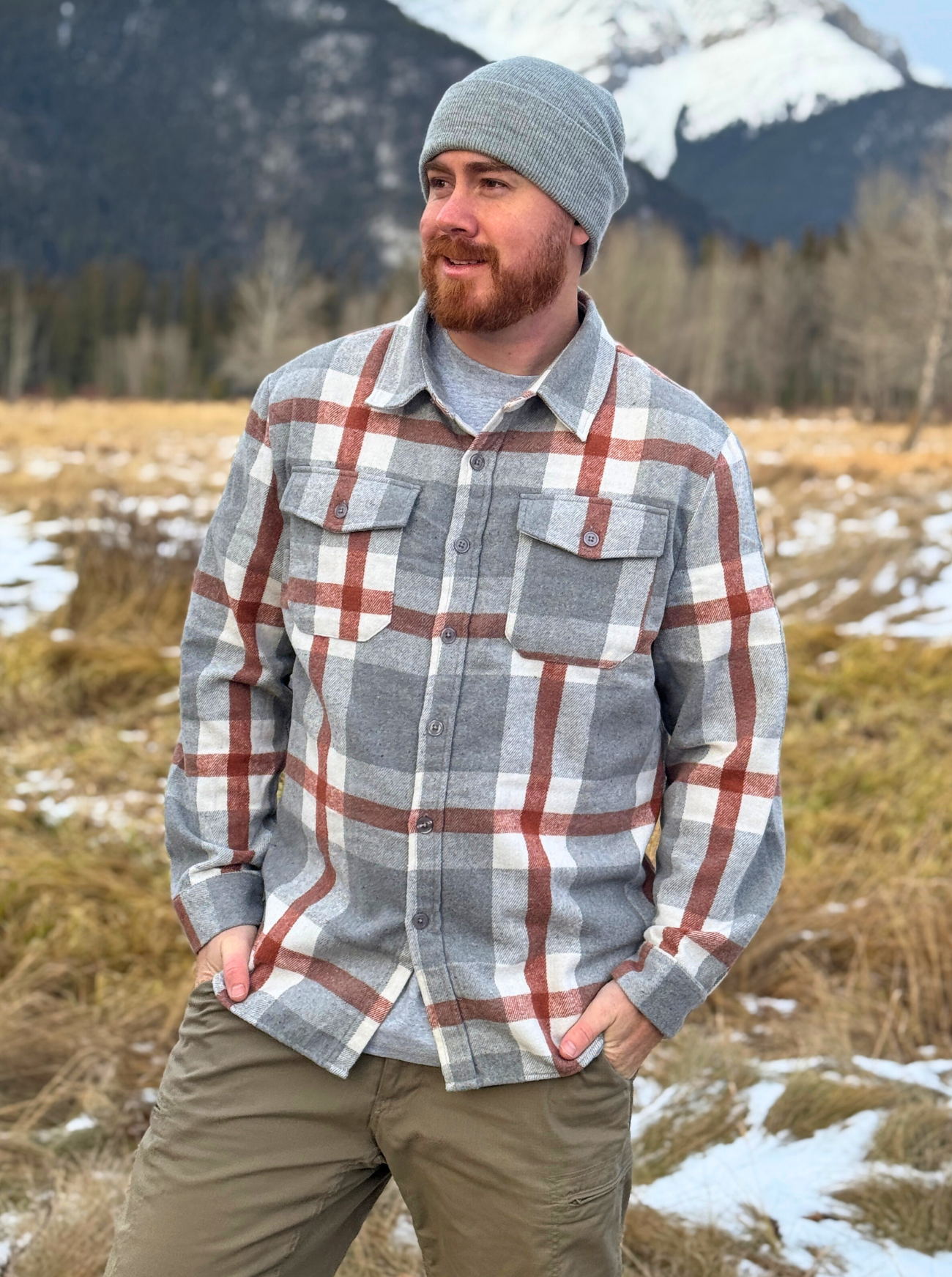 Man wearing a plaid flannel shirt and beanie standing in a snowy landscape in Banff, Canada