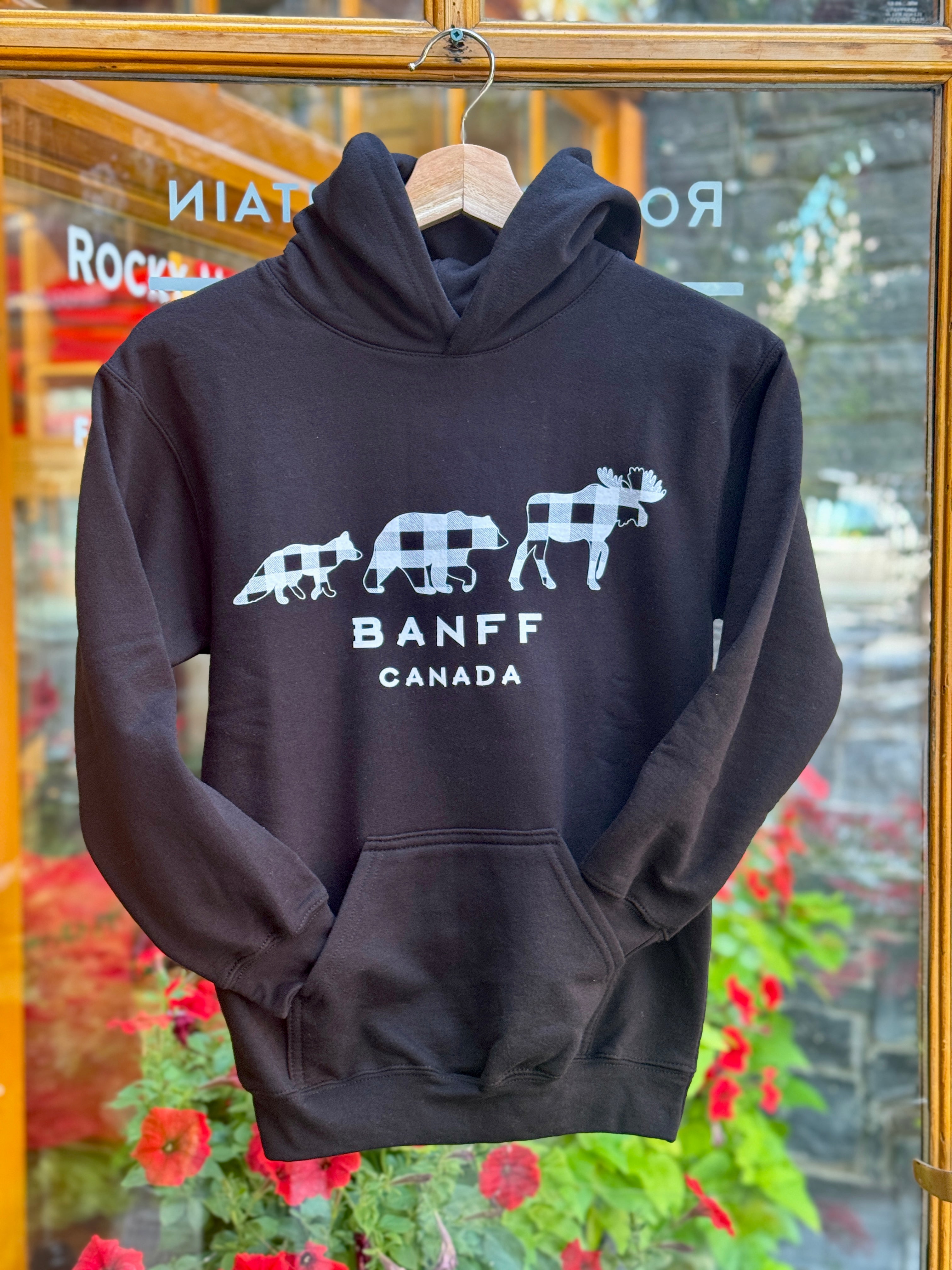 Black hoodie with white graphics and text 'Banff Canada' on a hanger in front of a glass door.
