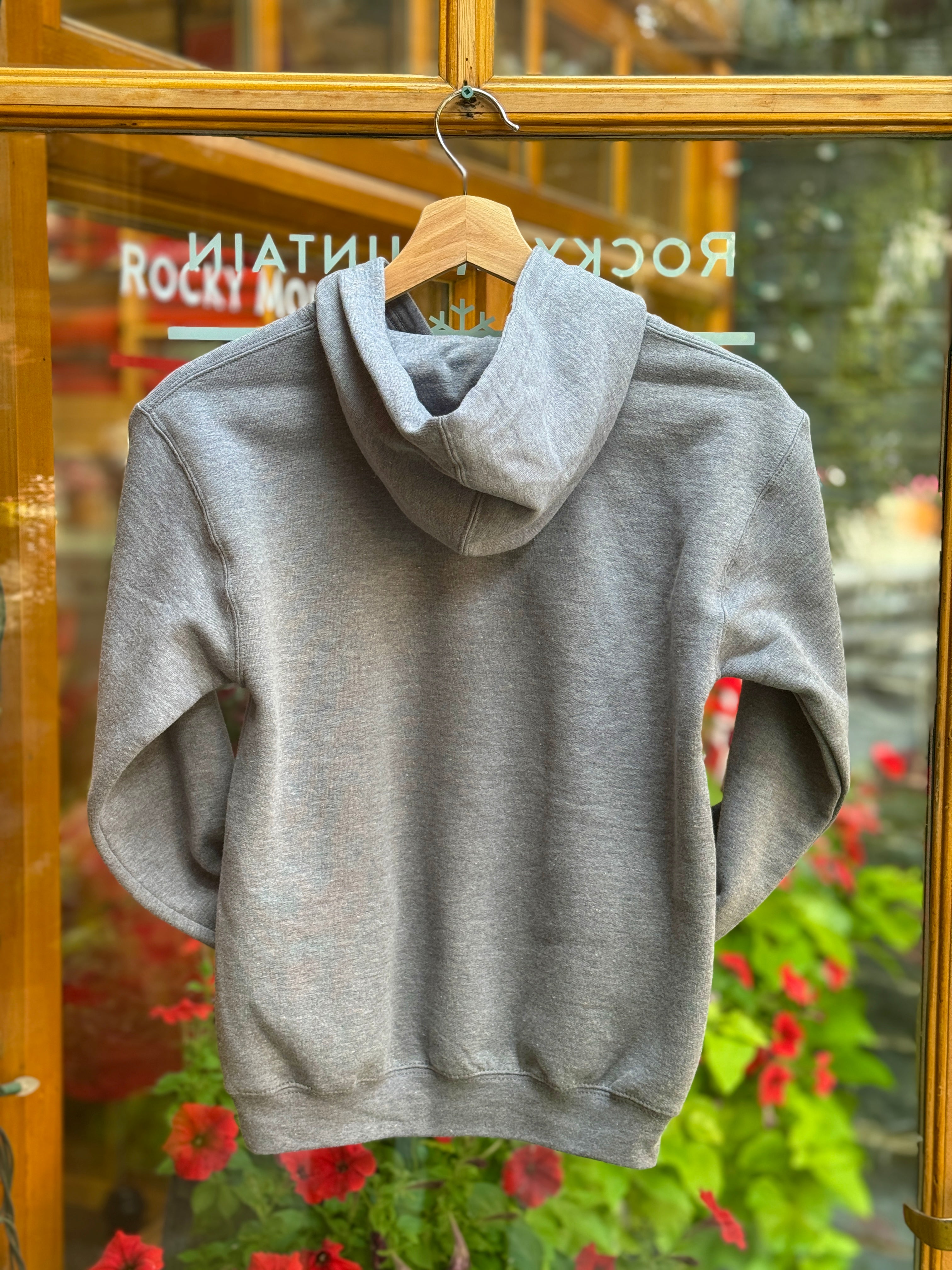 Kids grey hoodie on a hanger with a blurred background of flowers and glass