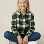Young girl wearing a plaid shirt and jeans sitting on the floor against a plain background