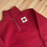 Kids Red pullover with a Canadian flag patch on a wooden surface