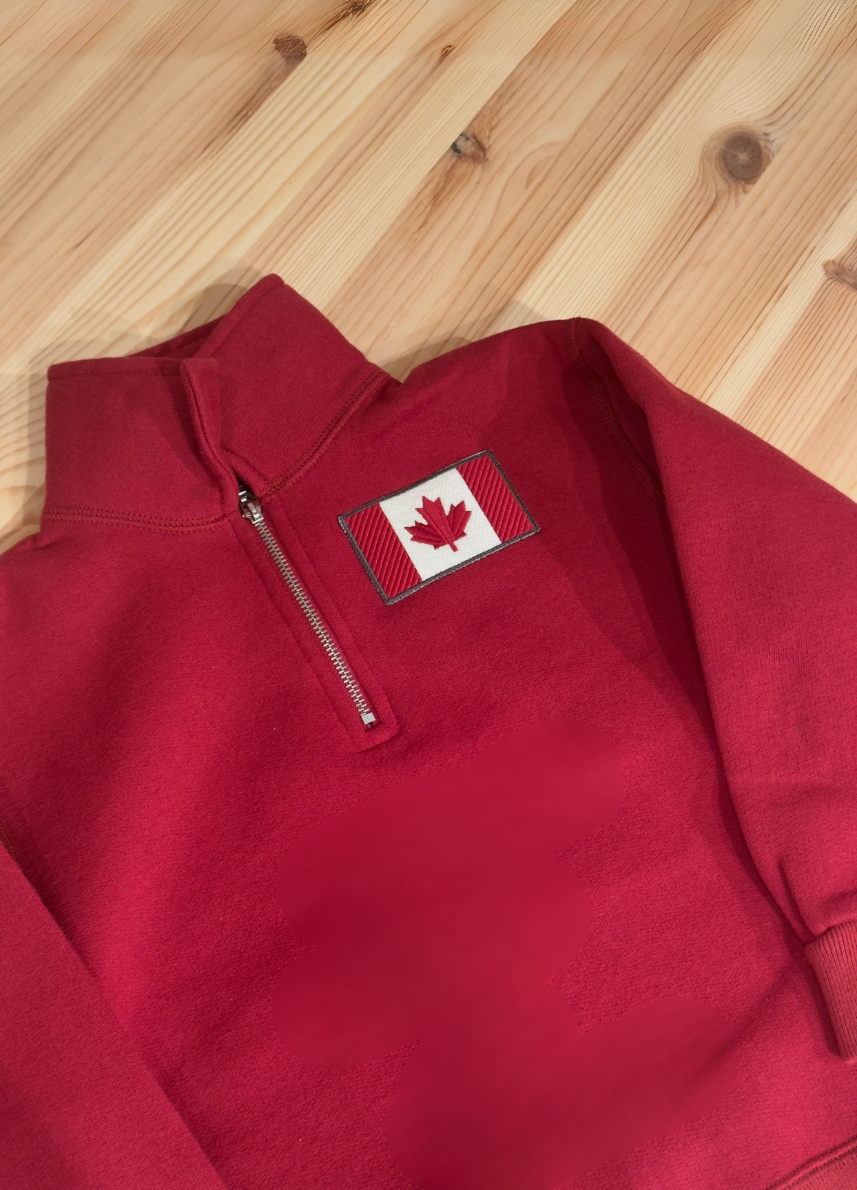 Kids Red pullover with a Canadian flag patch on a wooden surface