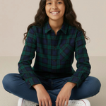 Young girl sitting cross-legged wearing a black watch tartan shirt and blue jeans on a beige background