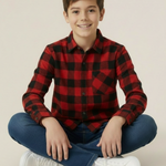 Young boy wearing a red and black buffalo check shirt sitting on the floor against a plain background