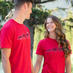Two people wearing red t-shirts outdoors.
