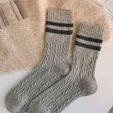 Pair of grey wool socks with black stripes on a textured surface.