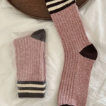 Pair of rose socks with black and white striped cuffs on a light surface.