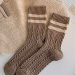 Pair of brown wool socks with cream stripes on a textured surface.