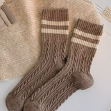 Pair of brown wool socks with cream stripes on a textured surface.
