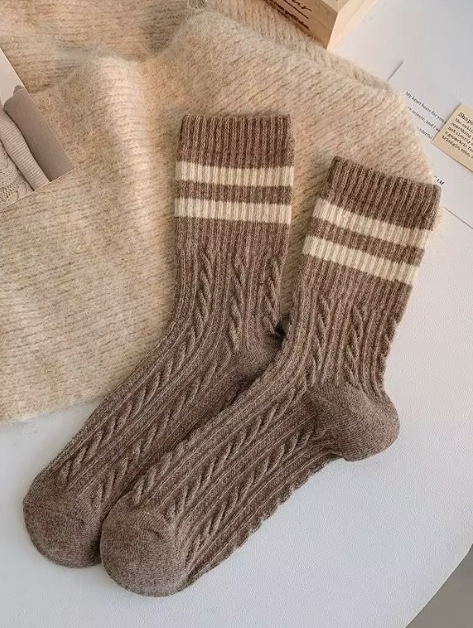 Pair of brown wool socks with cream stripes on a textured surface.