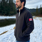 Man wearing a dark jacket with a Canadian flag patch in a snowy landscape.