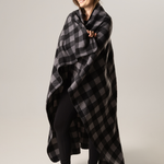 Woman wrapped in a black and gray checkered blanket against a plain background