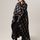 Woman wrapped in a black and gray checkered blanket against a plain background