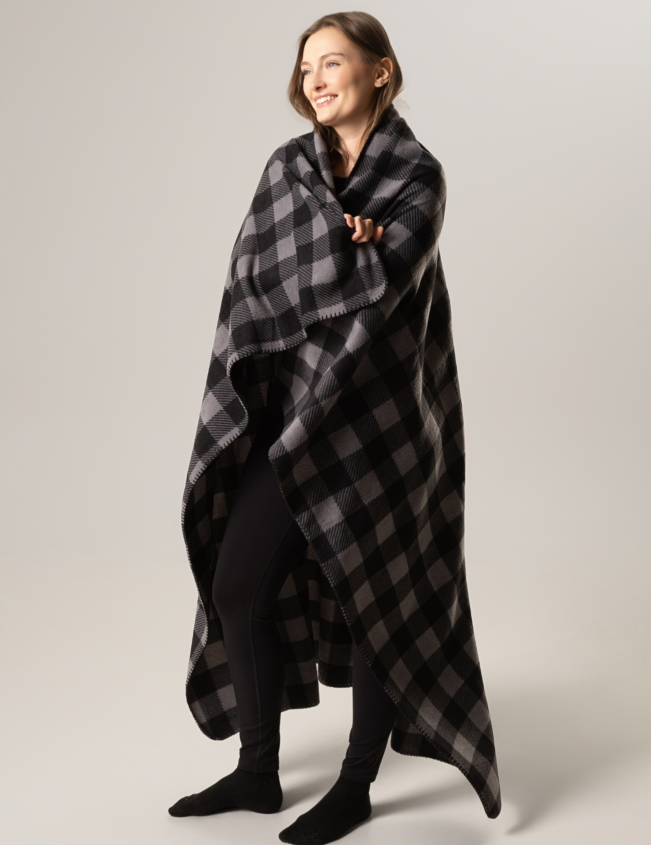 Woman wrapped in a black and gray checkered blanket against a plain background