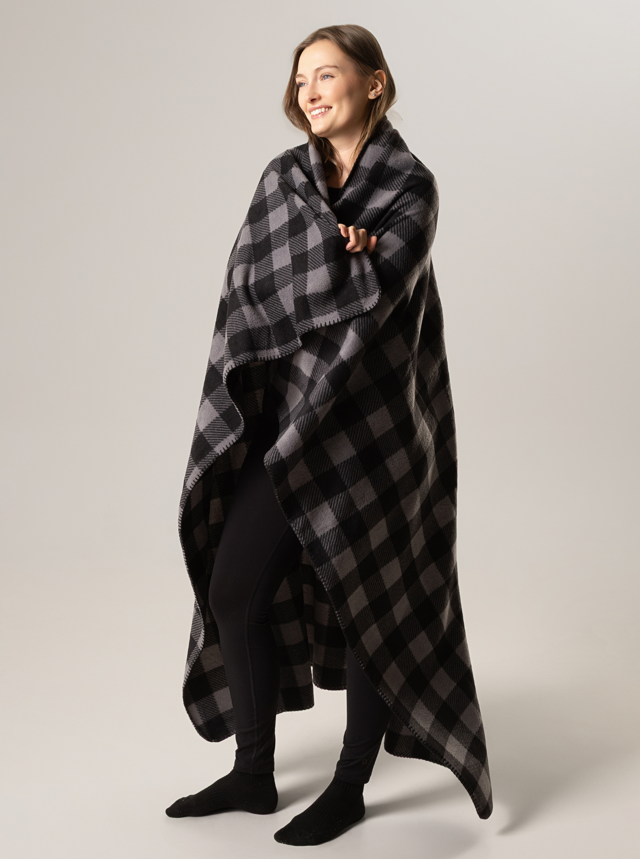 Woman wrapped in a black and gray checkered blanket against a plain background