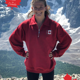 Person wearing a red pullover with a Canadian flag, standing in front of mountainous landscape.