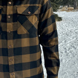 A man wearing a black and brown buffalo check flannel shirt with two flap breast pockets and two button cuff