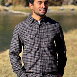 Man wearing a plaid flannel shirt standing outdoors by a river in Banff