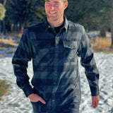 A man wearing a long-sleeved black and grey buffalo check flannel shirt with two breast pockets and a button cuff.