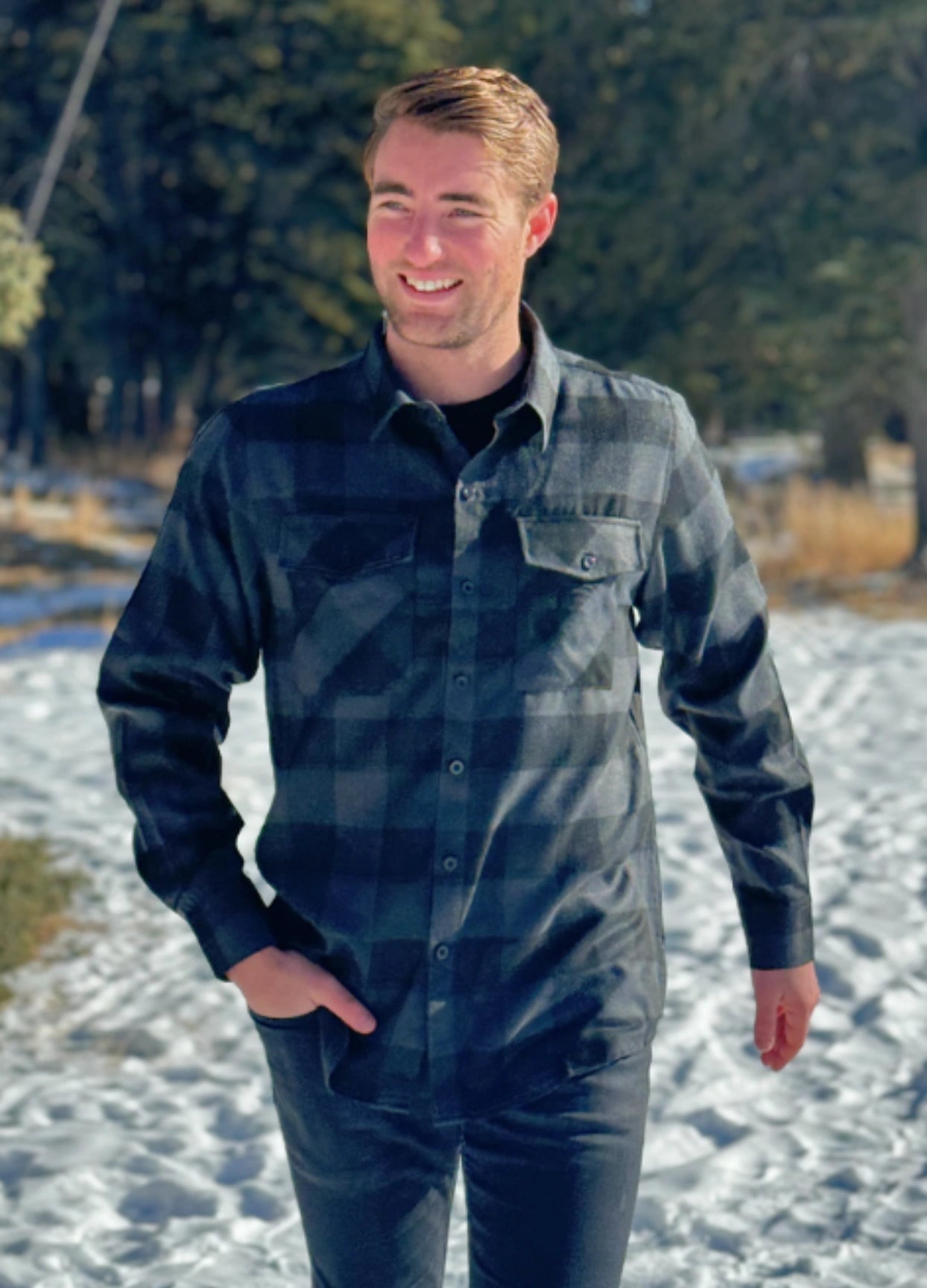 A man wearing a long-sleeved black and grey buffalo check flannel shirt with two breast pockets and a button cuff.