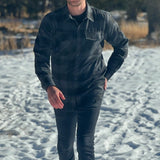 A man wearing a long-sleeved black and grey buffalo check flannel shirt with two breast pockets and a button cuff.