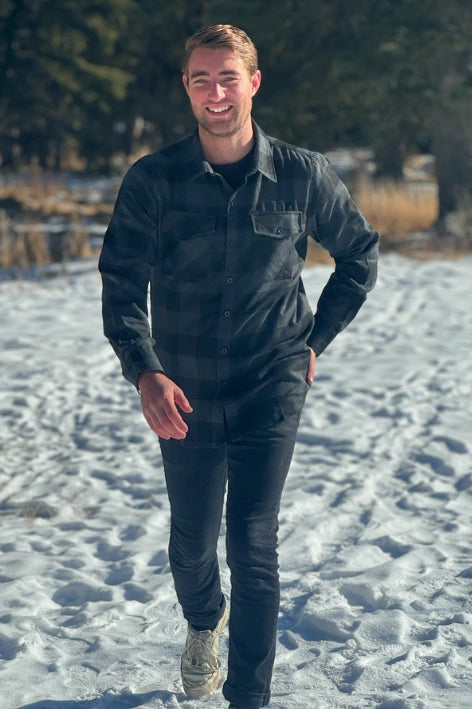 A man wearing a long-sleeved black and grey buffalo check flannel shirt with two breast pockets and a button cuff.