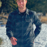 A man wearing a long-sleeved black and grey buffalo check flannel shirt with two breast pockets and a button cuff.