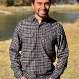 Man wearing a plaid flannel shirt standing outdoors with a river and trees in the background in Banff National Park