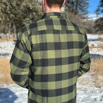 Back view of a man wearing a black and olive buffalo check flannel shirt with two flap breast pockets and a two button cuff.