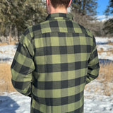 Back view of a man wearing a black and olive buffalo check flannel shirt with two flap breast pockets and a two button cuff.